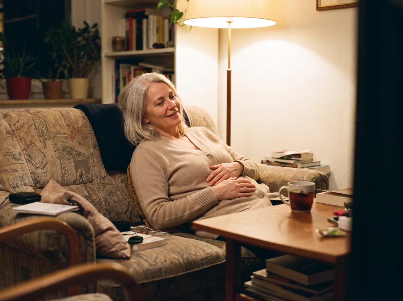 Frau sitzt abends entspannt auf dem Sofa